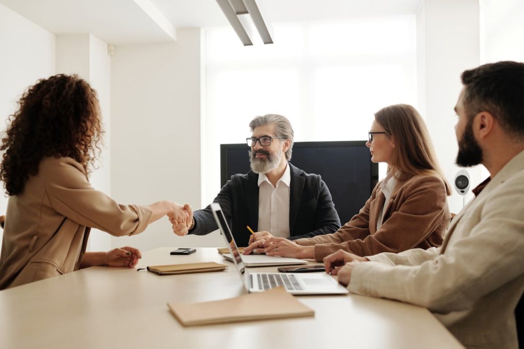 man-in-black-suit-jacket-sitting-beside-woman-in-brown-long-sleeve-shirt-4344860 Colleagues in an office celebrating a successful negotiation with a handshake.